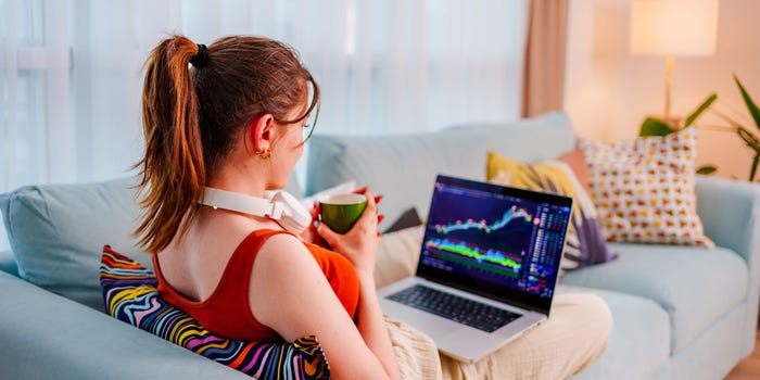 Woman looks if the stock market is open today while laying on the coach with a laptop.