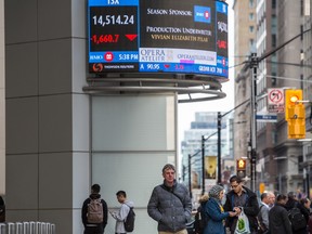 People walk by a screen displaying devalued stocks and the Toronto Stock Exchange at King and Bay Streets in Toronto, Ont.