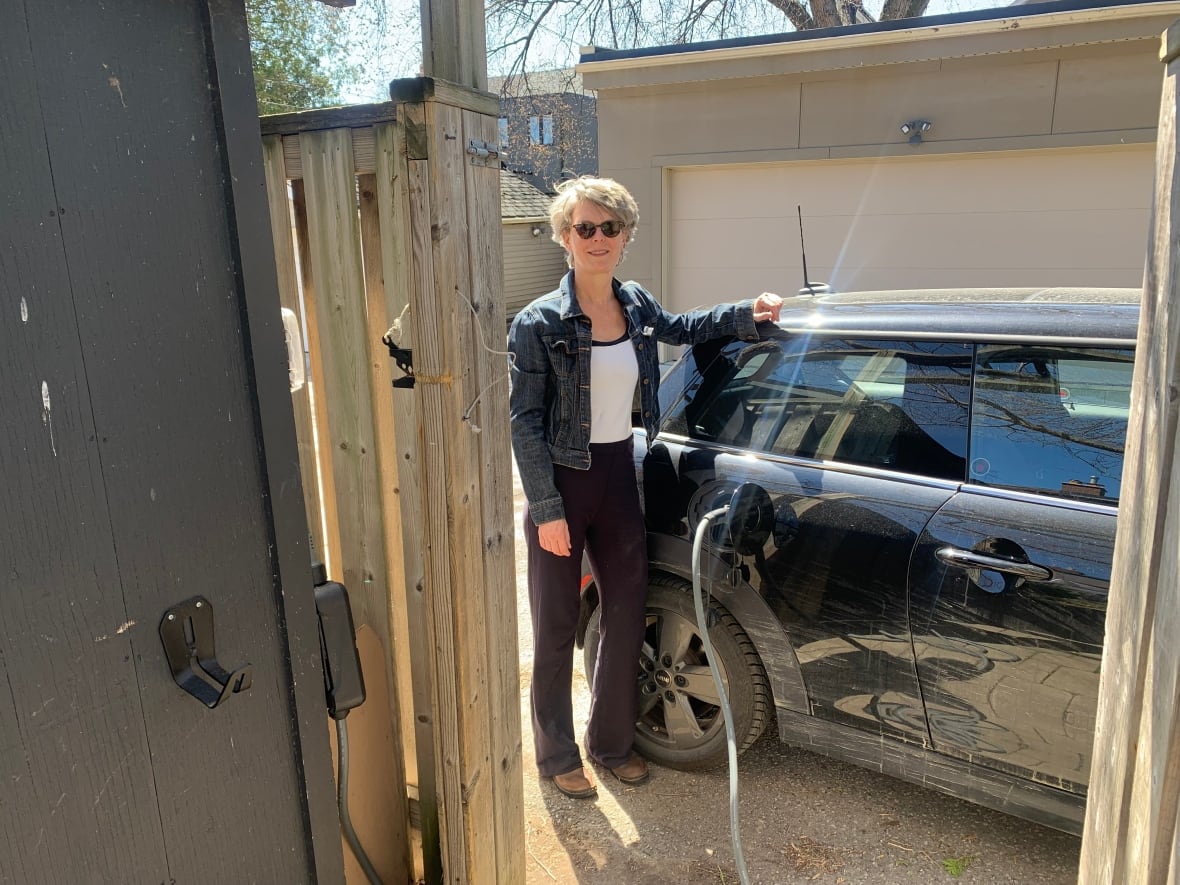 Woman standing beside car that is plugged in for charging